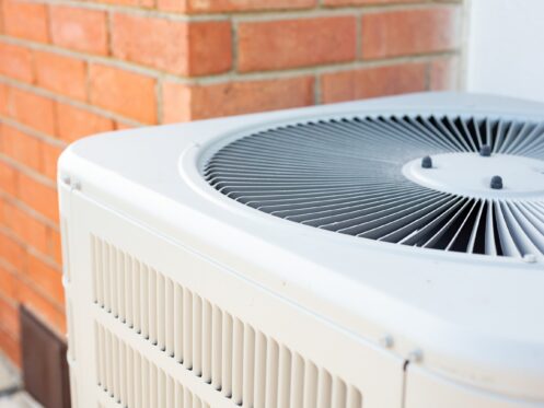 A view of an air conditioner condenser unit in the backyard of a home.