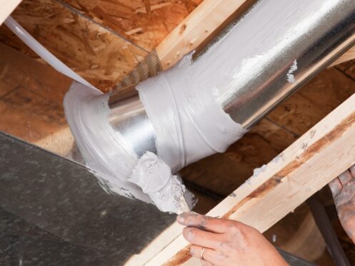 Man spreading caulk over a house air duct joint.